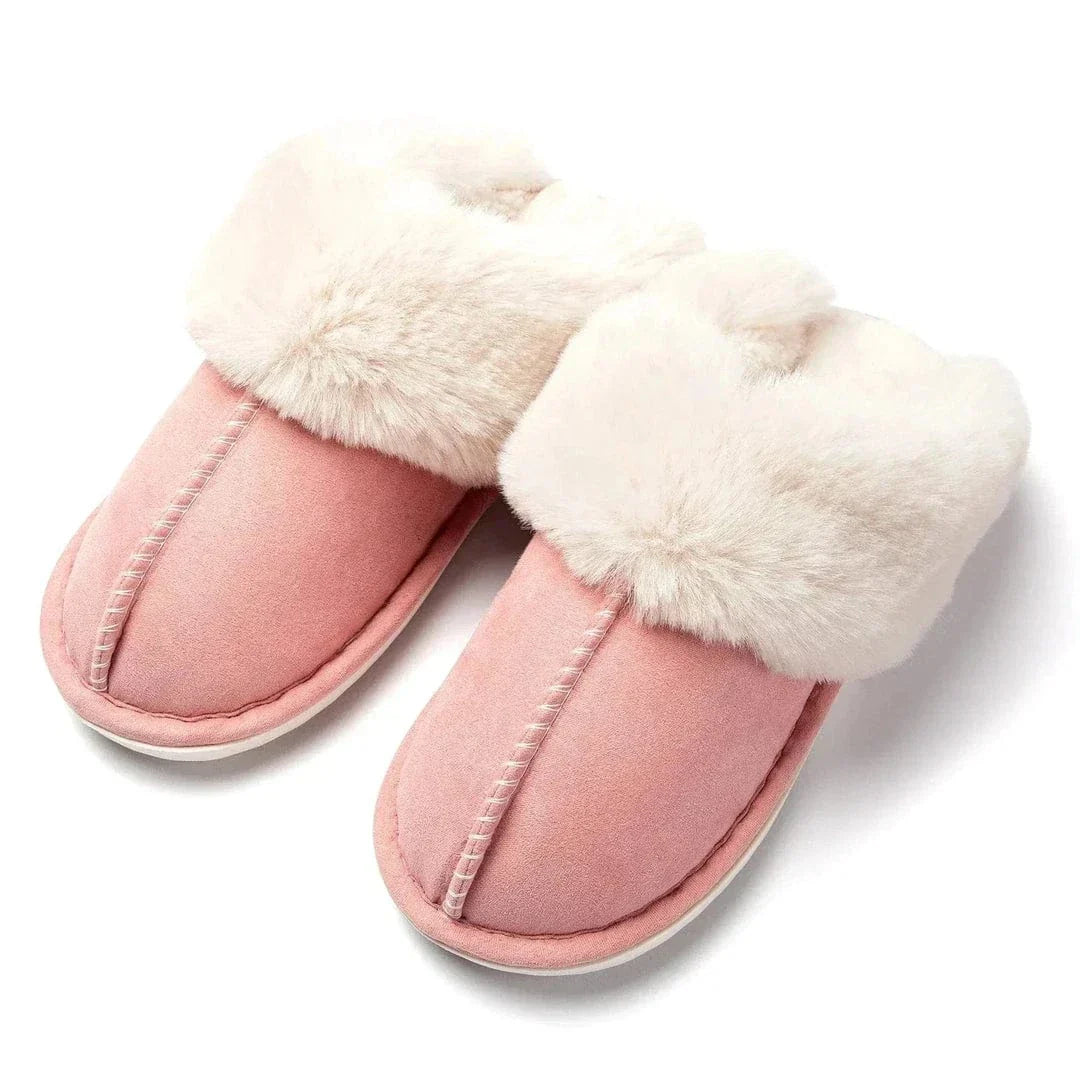 Pari vaaleanpunaisia tossuja, joissa on paksu, pörröinen valkoinen turkisreunus ja näkyvät ompeleet yläreunassa, asetettuina vierekkäin valkoisella taustalla.